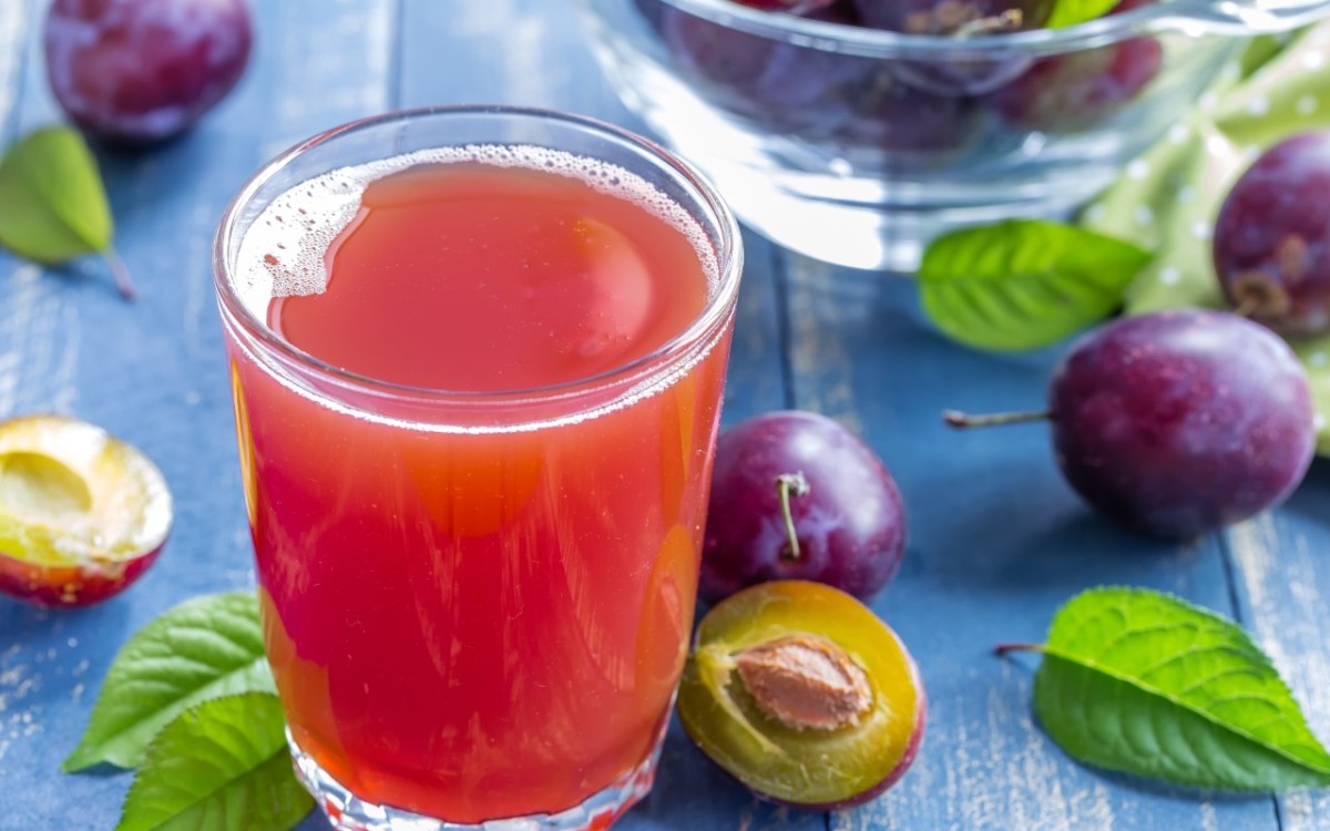 Ein Glas selbst gemachter Pflaumensaft. Drumherum liegen frische Pflaumen.