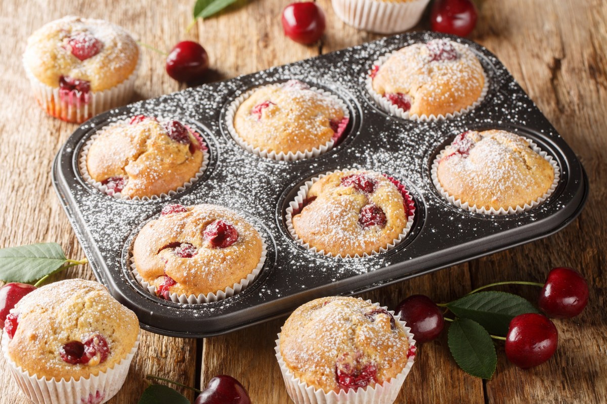 Ein 6-er Muffinblech mit Quark-Muffins mit Kirschen, daneben frische Kirschen und mehr Muffins.