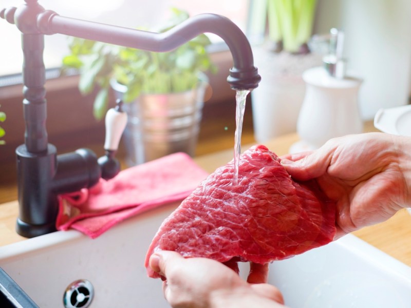 Ein rohes Stück Fleisch wird unter dem Wasserhahn gewaschen.