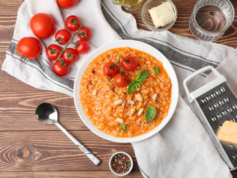 Risotto mit Tomaten auf einem Holztisch, Tomaten und Küchenreibe daneben