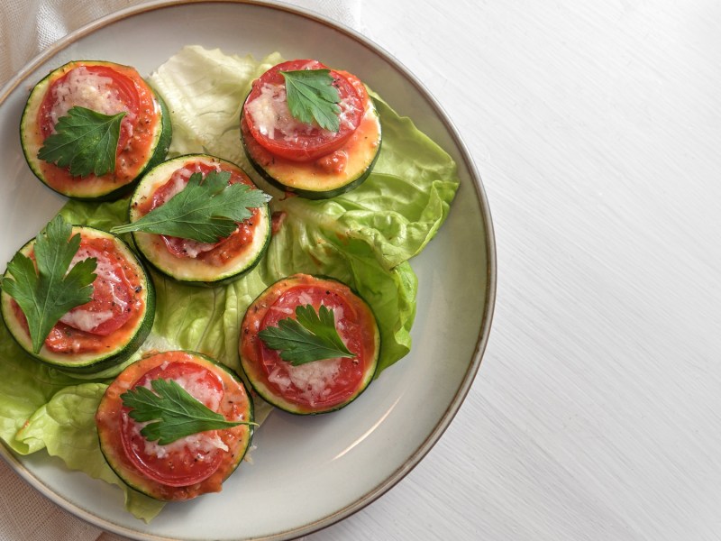 Zucchini-Bruschetta-Häppchen mit Parmesan und Tomate auf einem Teller, Draufsicht.