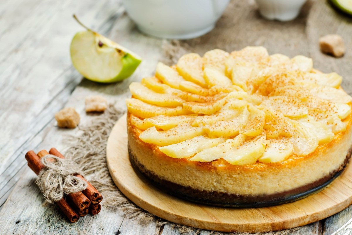 Ein Apfel-Karamell-Käsekuchen. Daneben liegen Zimtstangen.