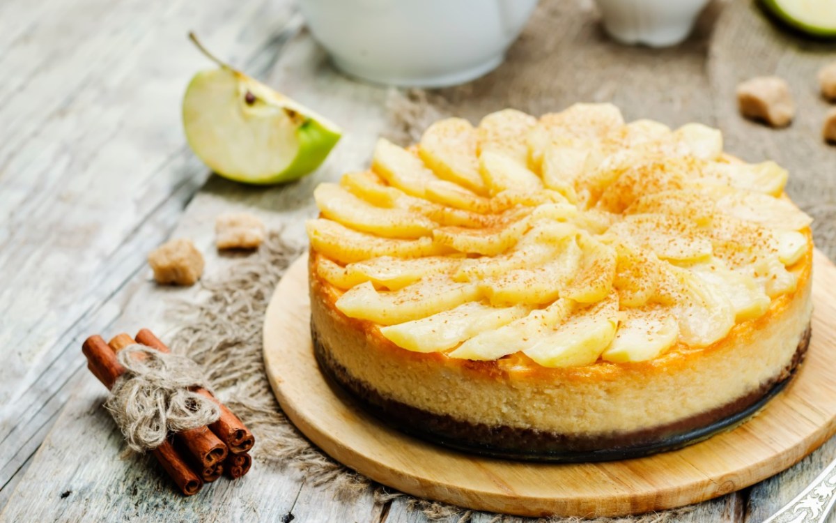 Ein Apfel-Karamell-Käsekuchen. Daneben liegen Zimtstangen.