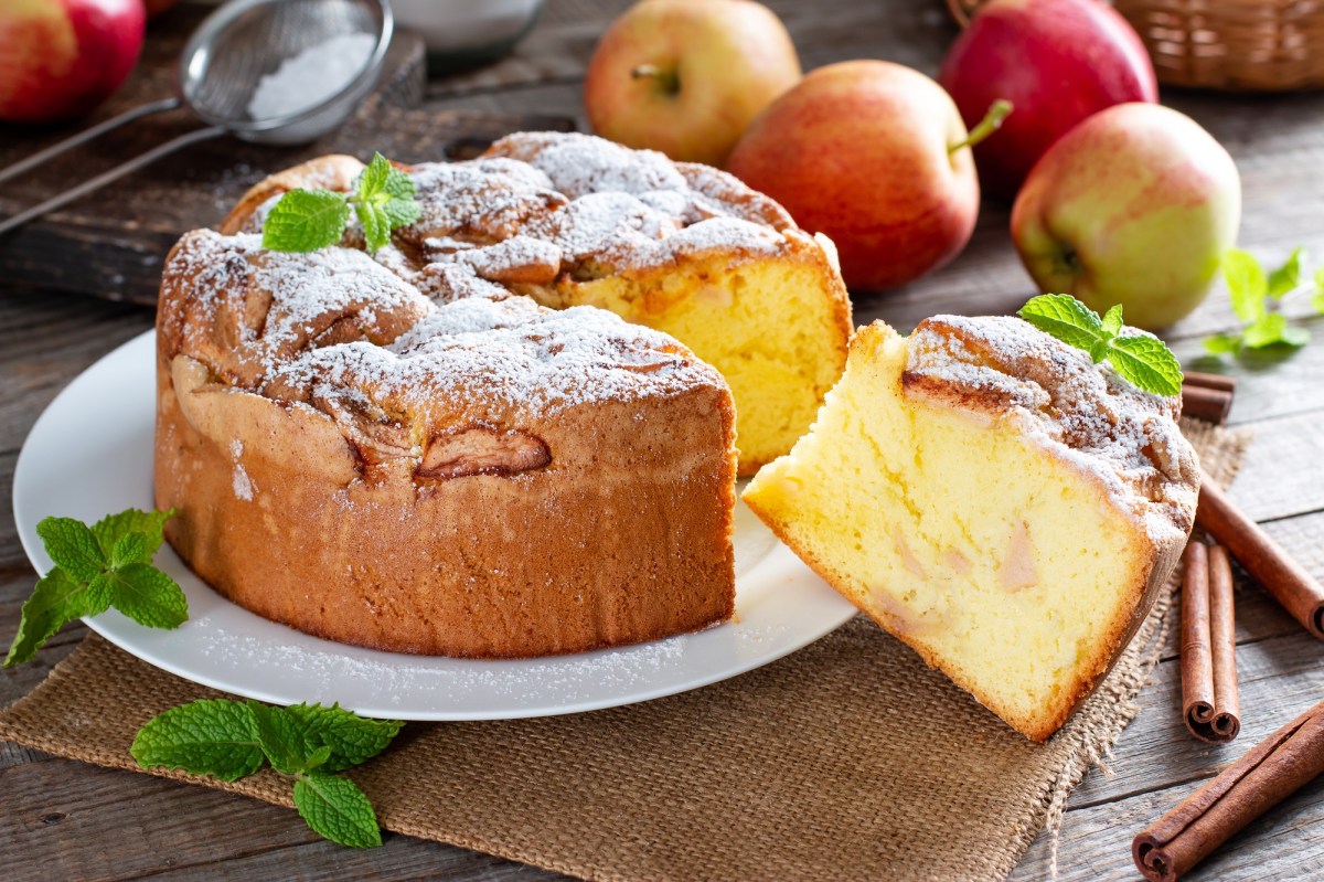 Angeschnittener italienischer Apfelkuchen Torta di Mele auf einem Teller. Drumherum Äpfel.