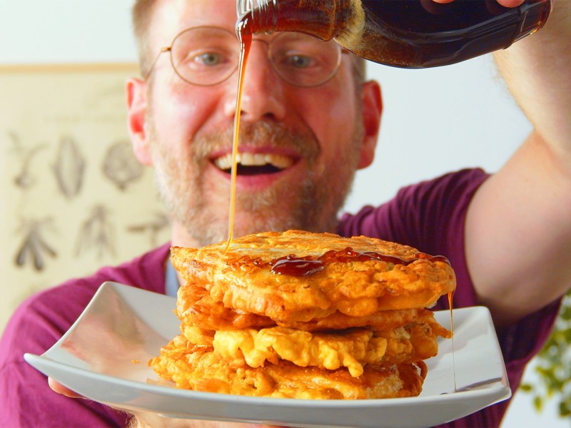 Ein Koch träufelt Sirup über einen Teller mit Kohl-Hackfleisch-Pancakes.