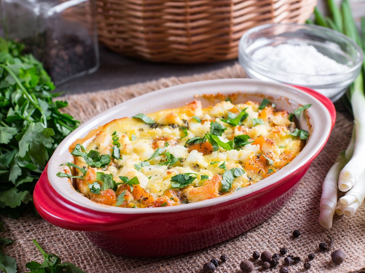 Kürbis-Gnocchi-Auflauf in ovaler, roter Auflaufform, daneben einige frische Zutaten.