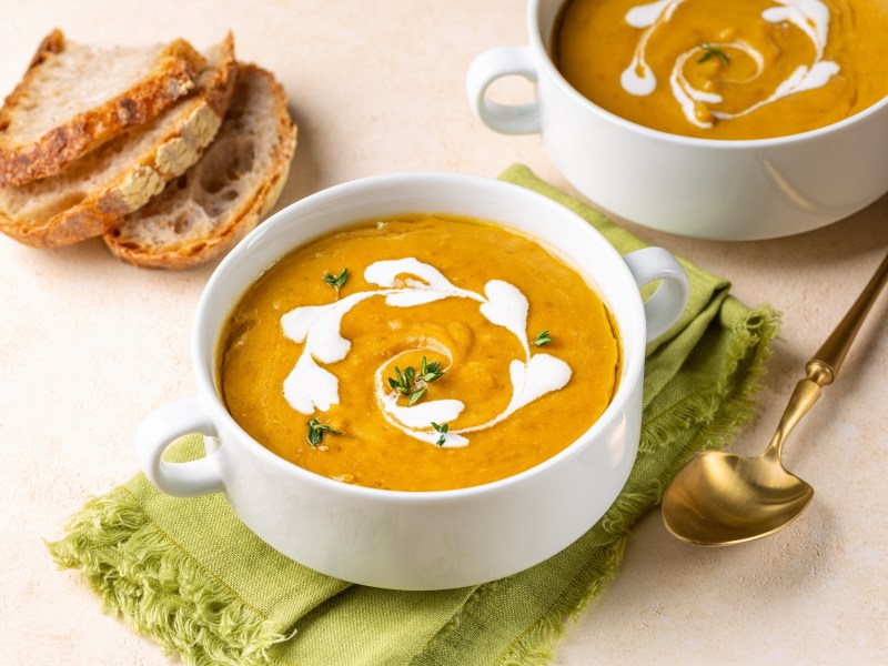 Zwei Schalen mit Kürbis-Linsen-Suppe auf einem Tisch.