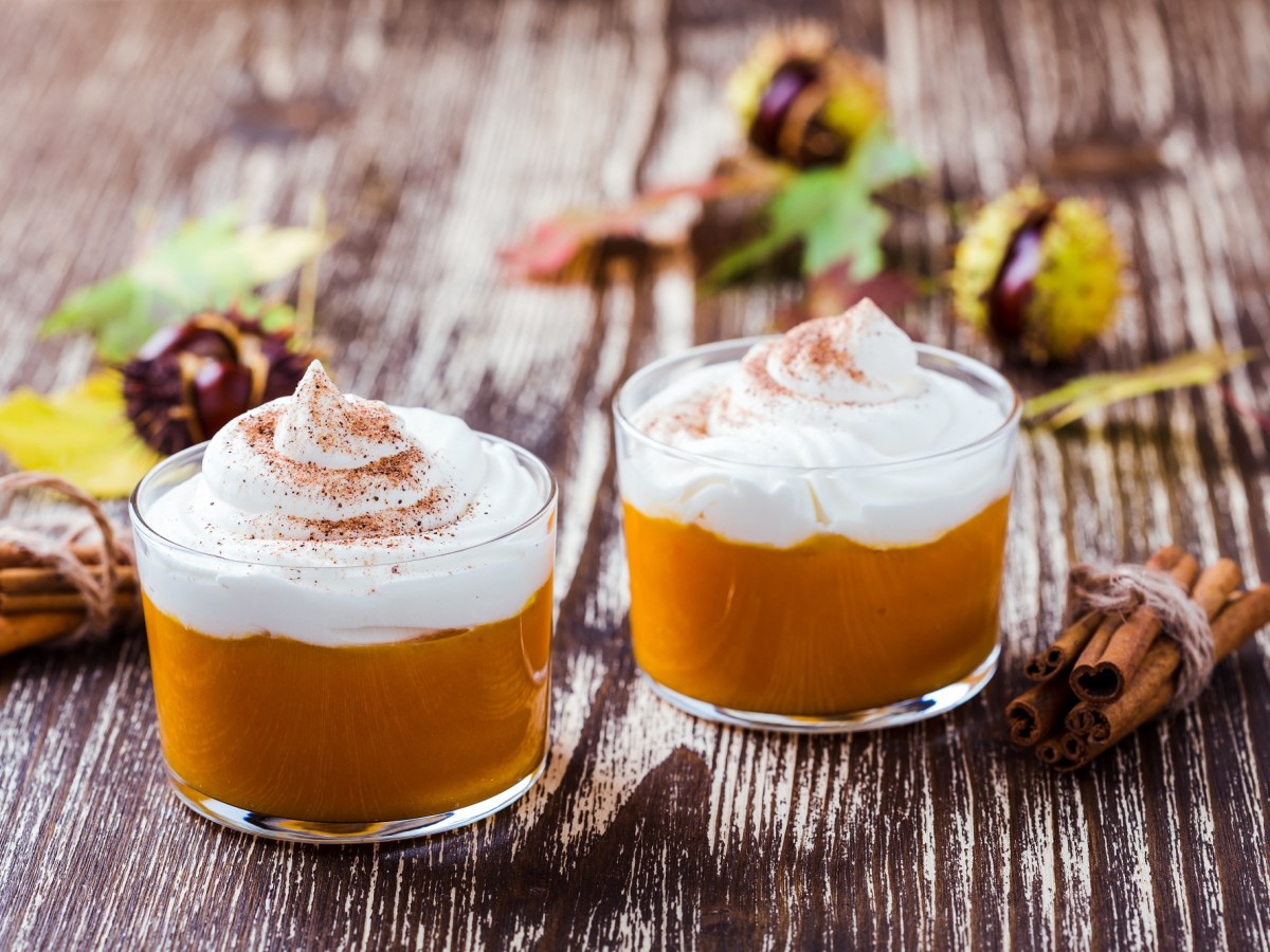 zwei Gläser Kürbis-Mousse mit Sahnehaube und Zimt bestreut, drumherum Kastanien.