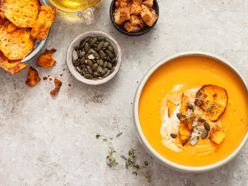 Schale mit Kürbis-Süßkartoffel-Suppe, Kürbiskernen und Süßkartoffelchips