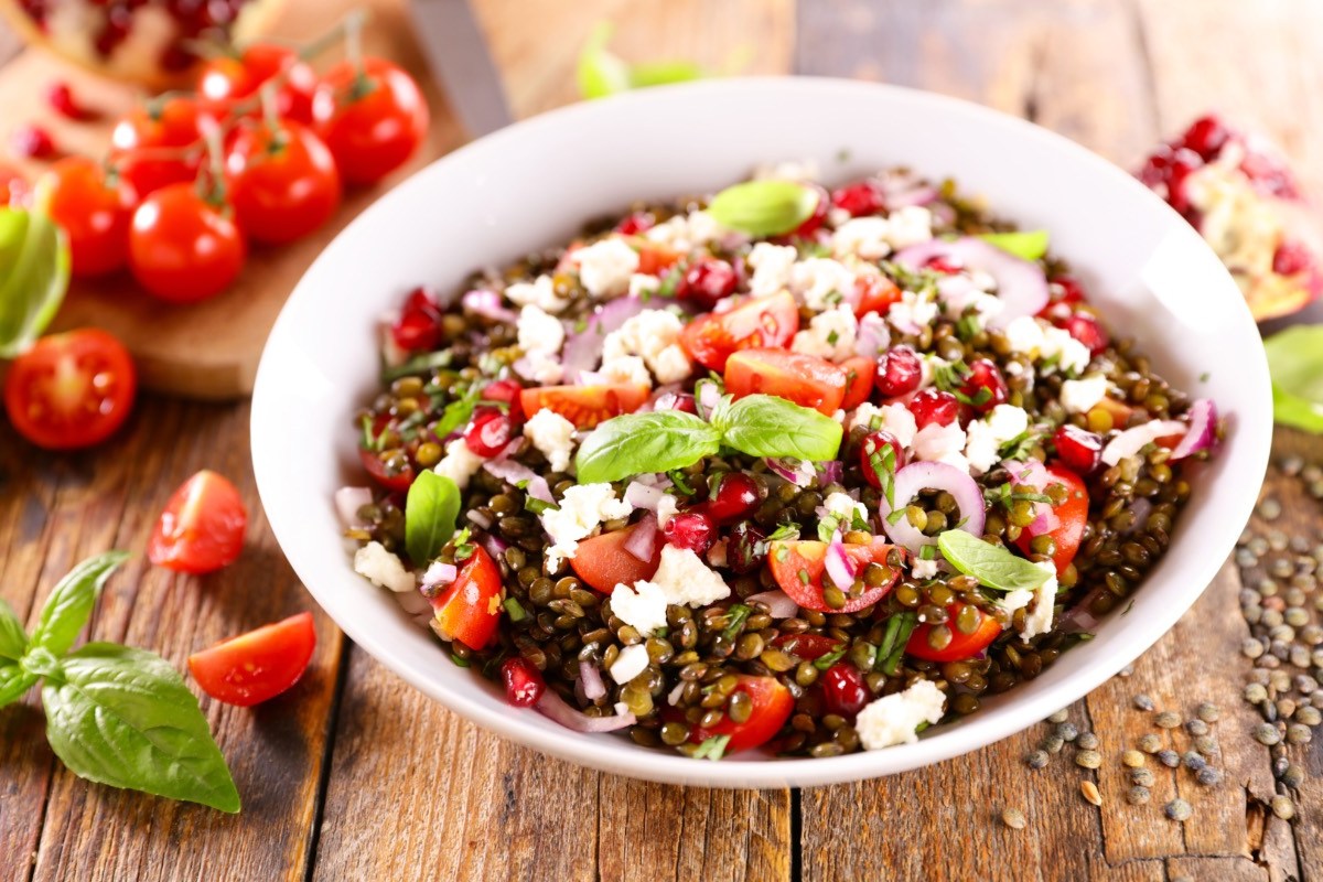 Eine Schüssel Linsensalat mit Feta. Daneben liegen frische Zutaten.