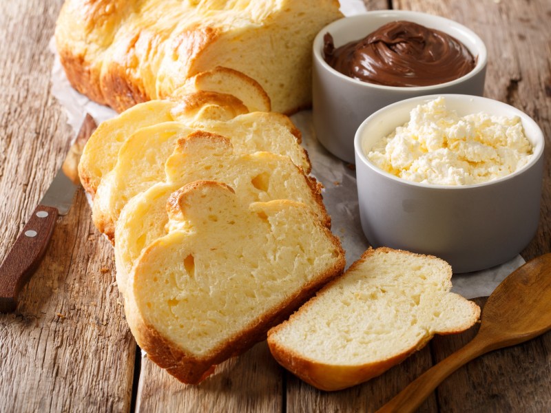 angeschnittenes Mascarpone-Brioche auf einem Holzbrett, Schokocreme daneben