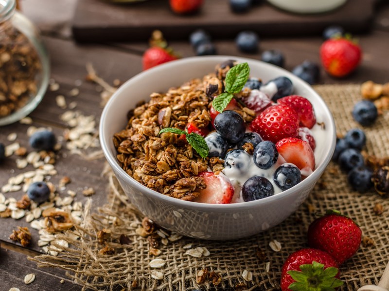 Eine Schüssel Müsli mit Joghurt und Balsamico-Beeren, drumherum verstreut die Zutaten.