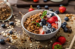 Eine Schüssel Müsli mit Joghurt und Balsamico-Beeren, drumherum verstreut die Zutaten.