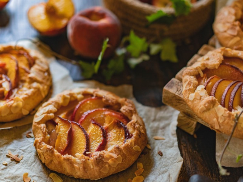 Mehrere Pfirsich-Galettes. Im Hintergrund liegen frische Pfirsiche.