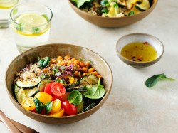 Quinoa-Kichererbsen-Bowl mit Zucchini, Tomaten und Spinat, daneben eine Schale Dressing.