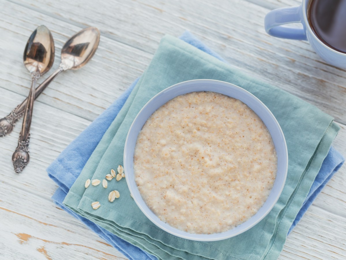 Schottischer Porridge in einer hellblauen Schüssel, daneben ligeen zwei Löffel.