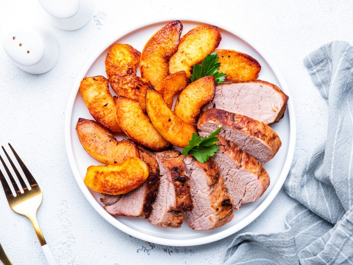 Angeschnittenes Schweinefilet mit geschmorten Äpfeln auf einem weißen Teller.