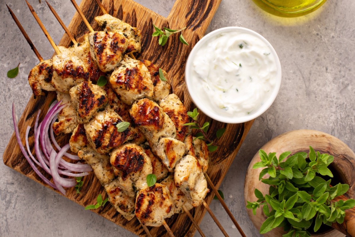 Mehrere Souvlaki. Daneben Zwiebeln und eine Schale mit Zaziki.