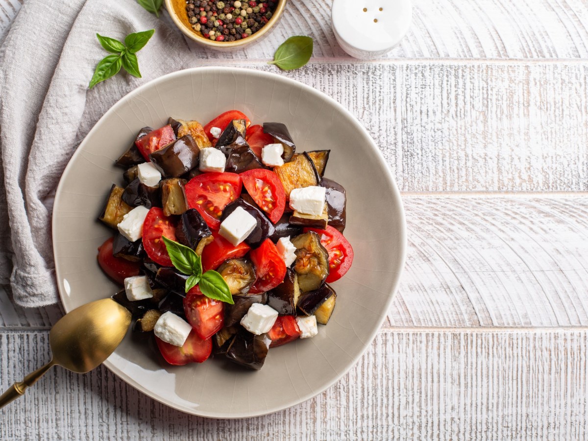 Tomatensalat mit Feta und Aubergine, angerichtet mit Basilikum, auf einem hellen Teller.