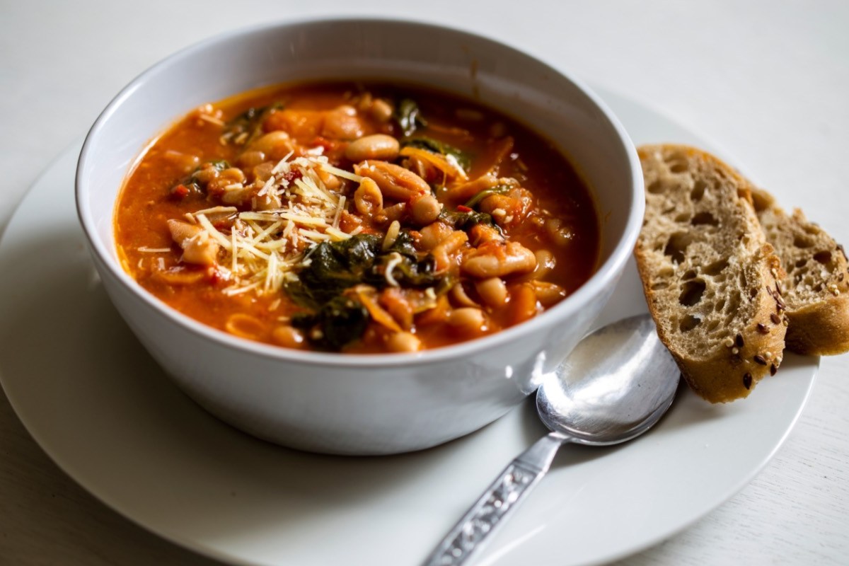 Eine Schüssel mit toskanischer Bohnensuppe. Daneben liegen eine Scheibe Brot und Löffel.