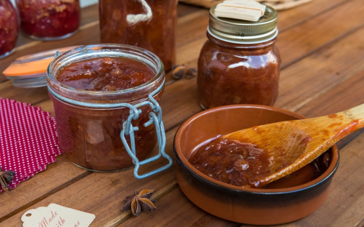 Mehrere Gläser Zwetschgen-Chitney. Daneben ein Holzlöffel mit Chutney, der in einer kleinen Schale liegt.