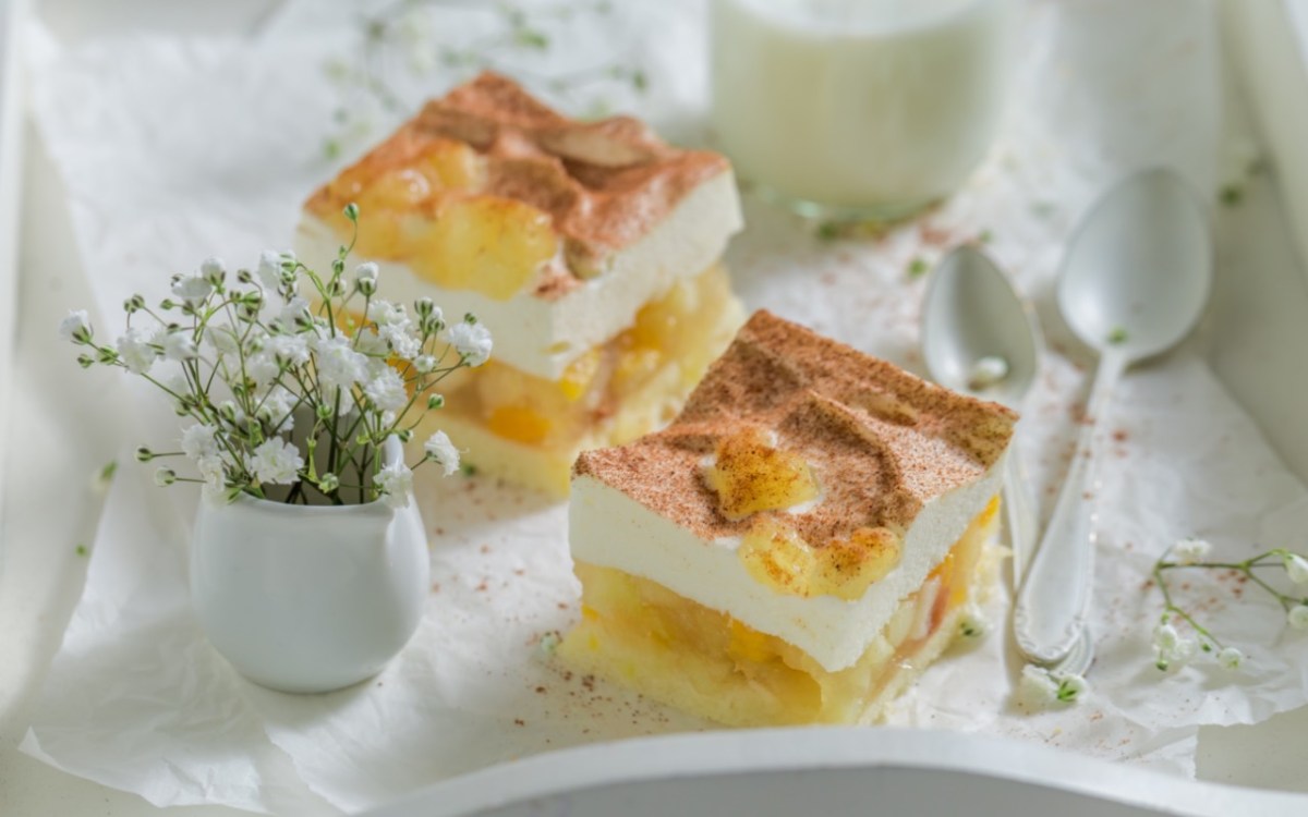 Zwei Stücke Apfel-Zimt-Torte auf einem Serviertablett. Daneben sind eine Vase mit Blumen und ein Löffel.