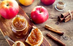 Ein Glas Bratapfelmarmelade. Daneben frische Äpfel und ein Brot mit Marmelade bestrichen.