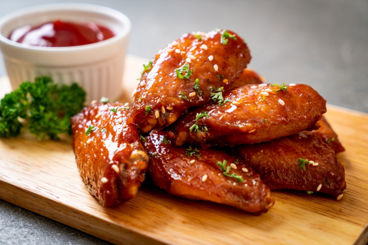 Ein paar Chicken Wings aus dem Airfryer aus einem Brett, bestreut mit Petersilie, daneben eine weiße Schale Ketchup.