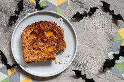 Halloween-Sandwich mit Käse und Kürbisgesicht auf einem Teller in der Draufsicht, drumherum Halloween-Deko.