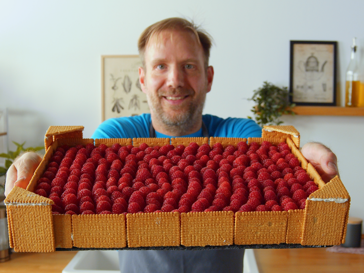 Ein Mann hält eine Himbeer-Buttercreme-Torte in die Kamera.