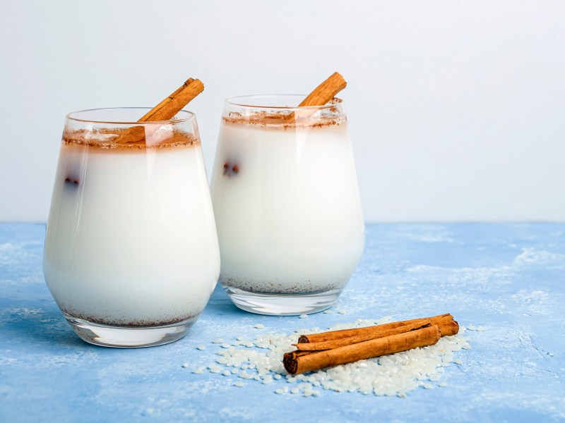 Zwei Gläser Horchata auf einem blauen Tisch, garniert mit Zimt und Zimtstangen.