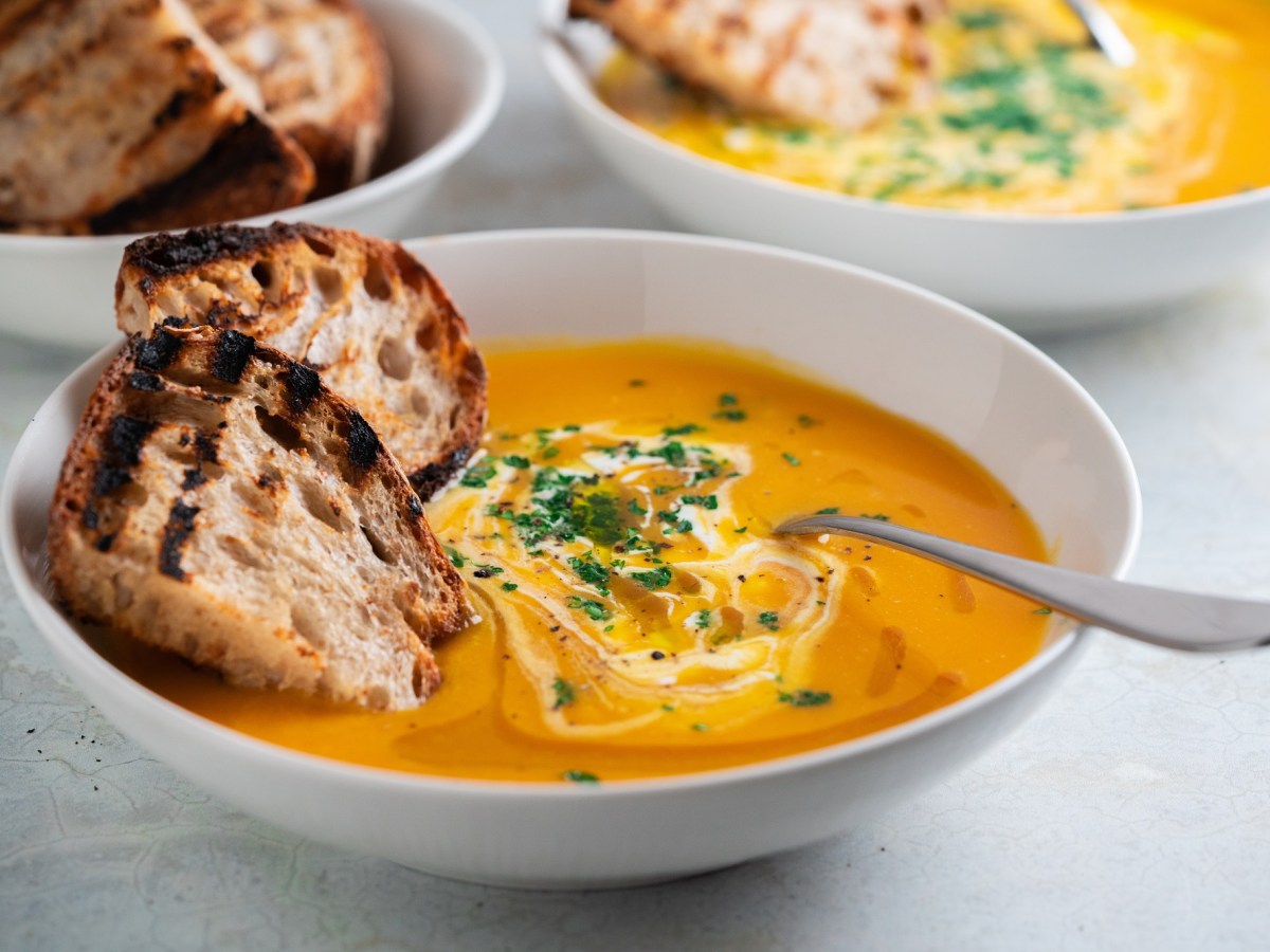 Eine Schüssel Kokos-Kürbissuppe mit Orangensaft und Brotscheiben.