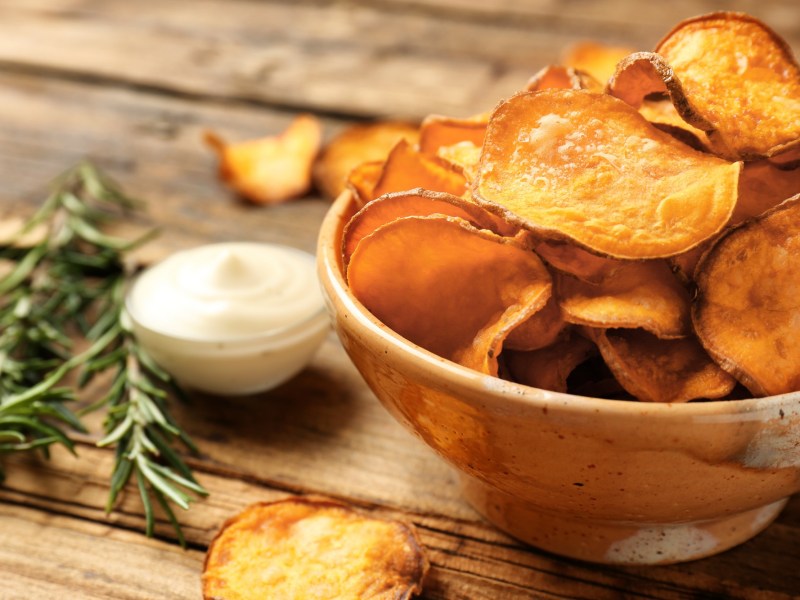 Eine Schüssel Kürbis-Chips, daneben eine Schale mit weißem Dip und ein paar Rosmarinzweige.