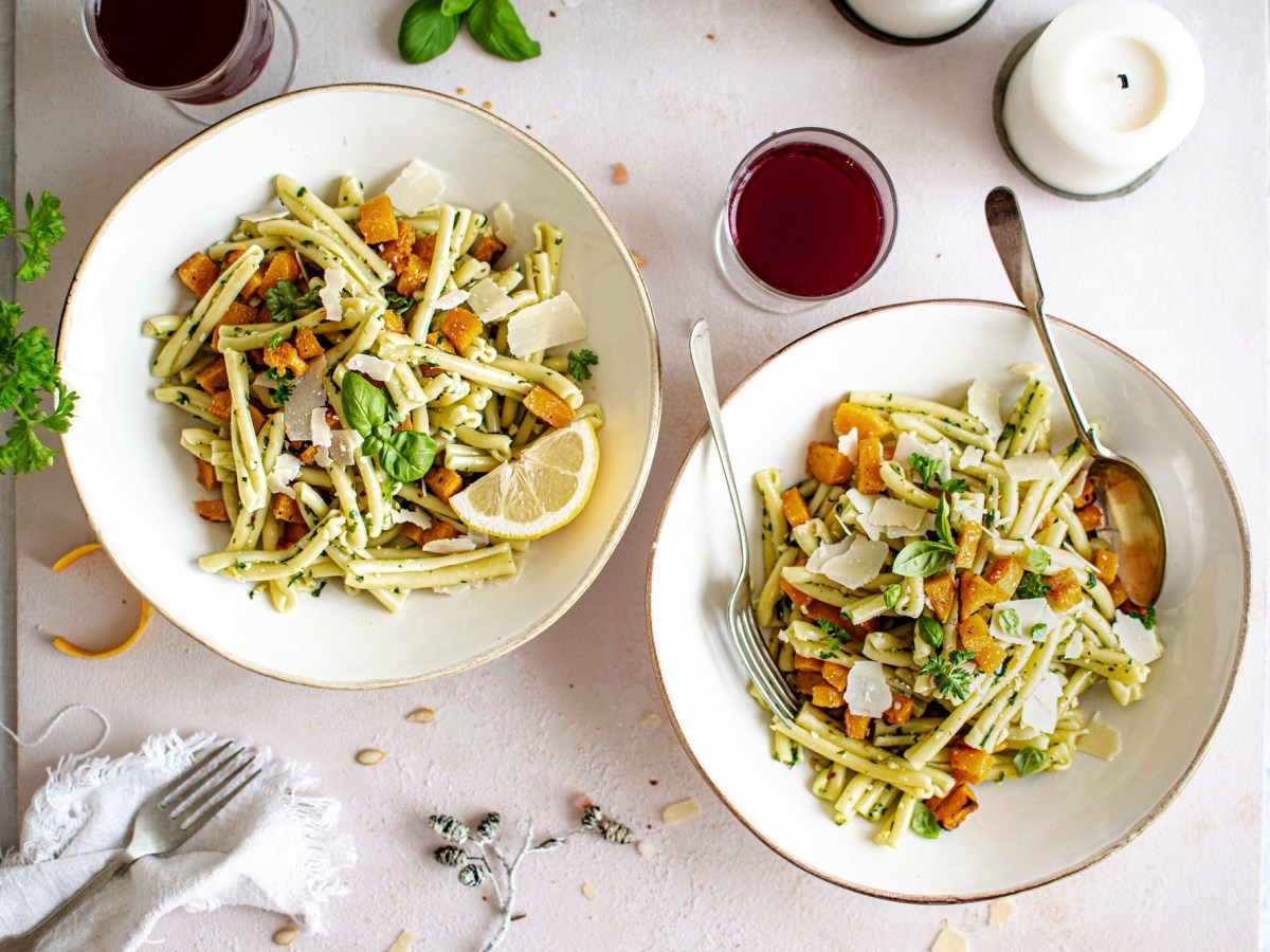 Zwei Teller Nudeln mit Kürbis und Pesto, serviert mit Parmesan.