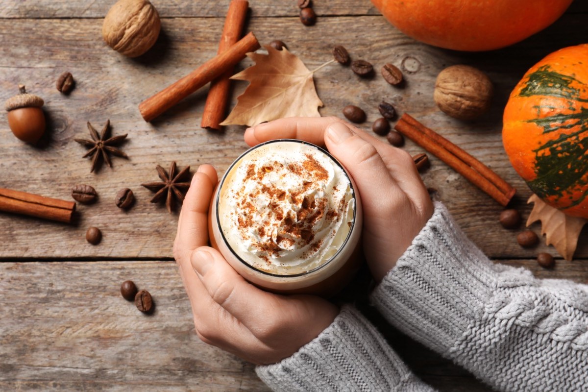 Pumpkin Spice selber machen: Eine Frau hält eine Tasse Kaffe mit Pumpkin Spice in den Händen. Drumherum liegen Zutaten.