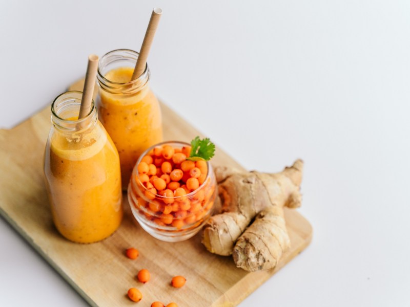 Zwei Gläser Sanddorn-Ingwer-Smoothie mit Sanddornbeeren und Ingwer daneben