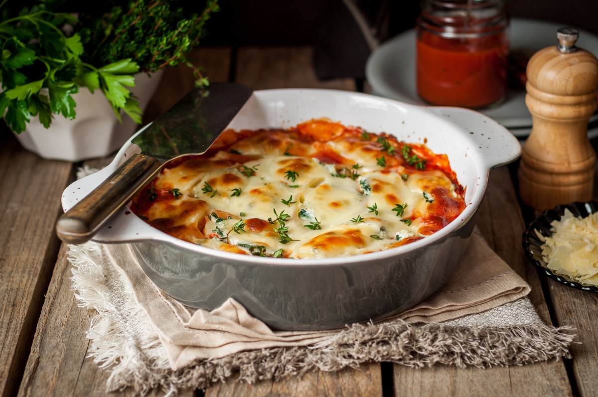 Weißkohl-Lasagne in runder Auflaufform auf einem Geschirrhandtuch, drumherum Gewürzstreuer, und Kräuter.