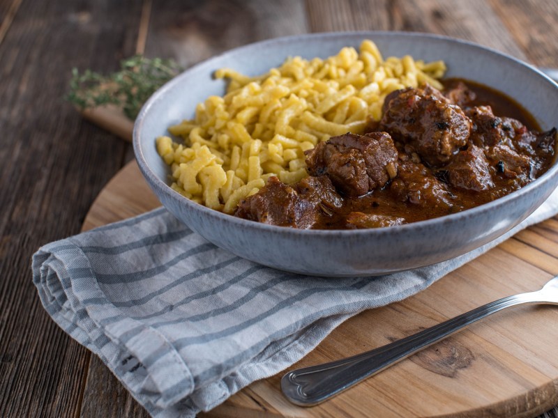 Ein Teller Wiener Saftgulasch mit Spätzle auf einem Geschirrtuch.