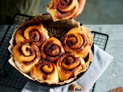 Zimtschnecken aus dem Airfryer in einer runden Form, eine wird herausgenommen.