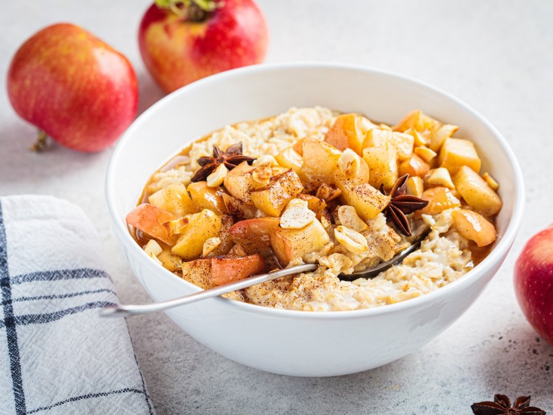 Eine Schale Bratapfel-Porridge mit gebratenen Äpfeln und Anissternen, drumherum Äpfel.