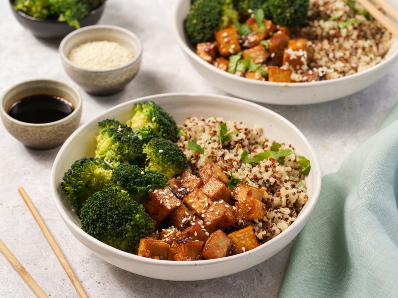 2 Brokkoli-Quinoa-Bowls mit gebratenem Tofu, daneben eine Schale Dressing.