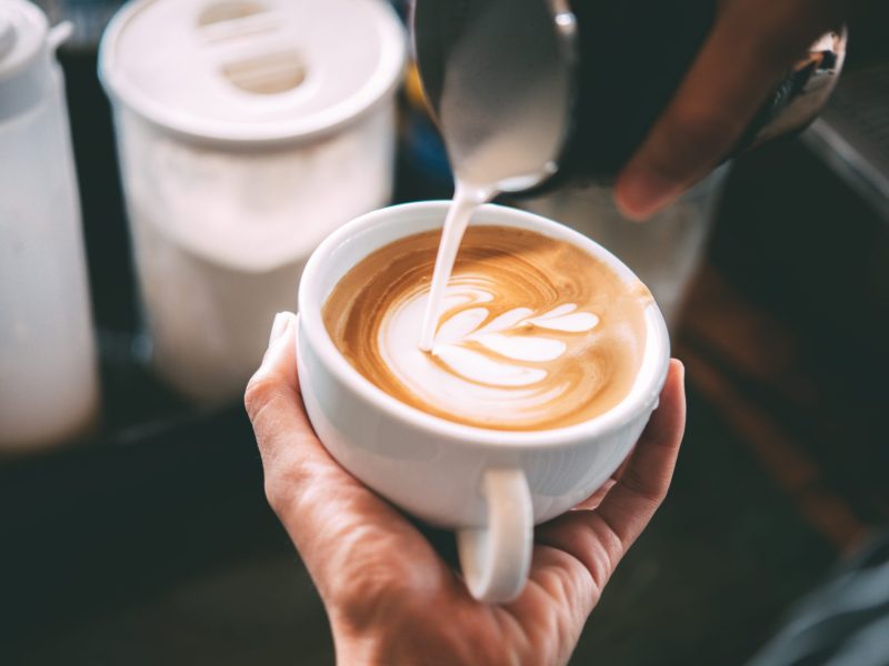 De'Longhi SiebtrÃ¤ger im Angebot bei Amazon: Ein Barista kippt Milch in eine Tasse Kaffee.