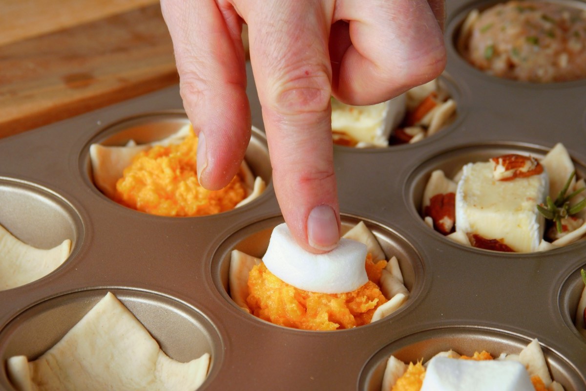 Fingerfood-Cups: Ein Marshmallow wird auf Kartoffelbrei aus Süßkartoffel in einem Muffinblech gedrückt.