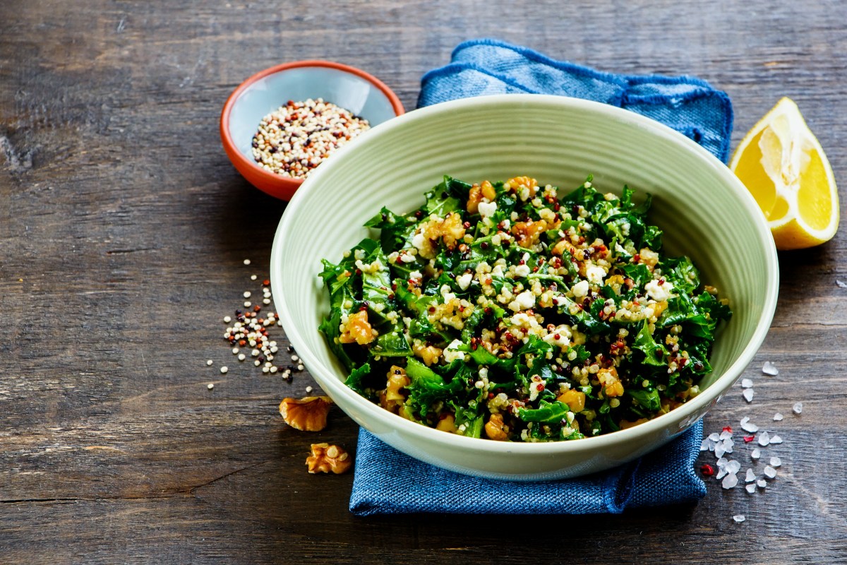 Eine Schüssel Grünkohlsalat mit Feta und Walnüssen, daneben eine angeschnittene Zitrone.