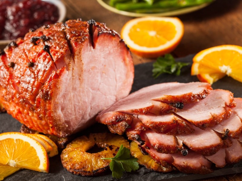 Ein Honey Glazed Ham mit karamellisierten Ananasscheiben, der zur HÃ¤lfte in Scheiben geschnitten wurde.