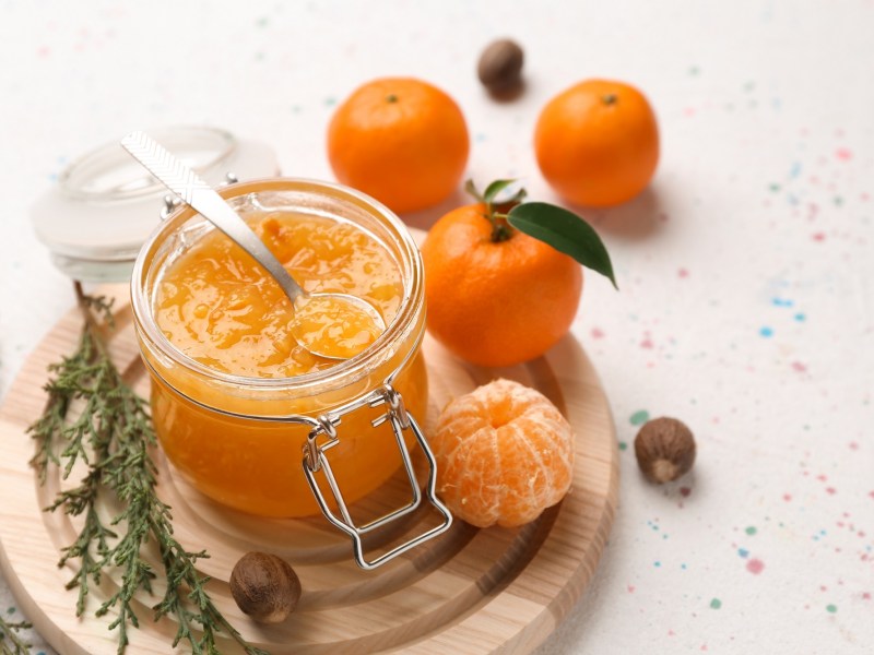 Glas Mandarinenmarmelade mit Mandarinen daneben