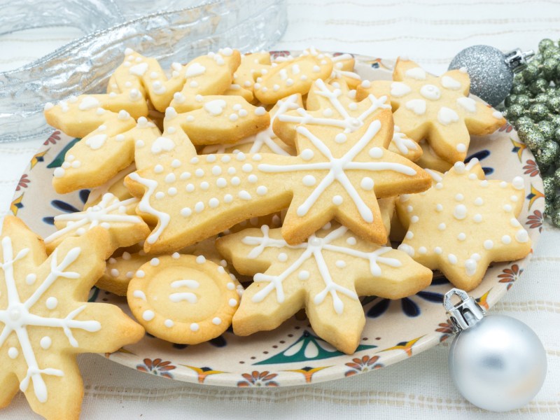 Ein Teller MarzipanplÃ¤tzchen verziert mit Zuckerguss, daneben Weihnachtsdeko.