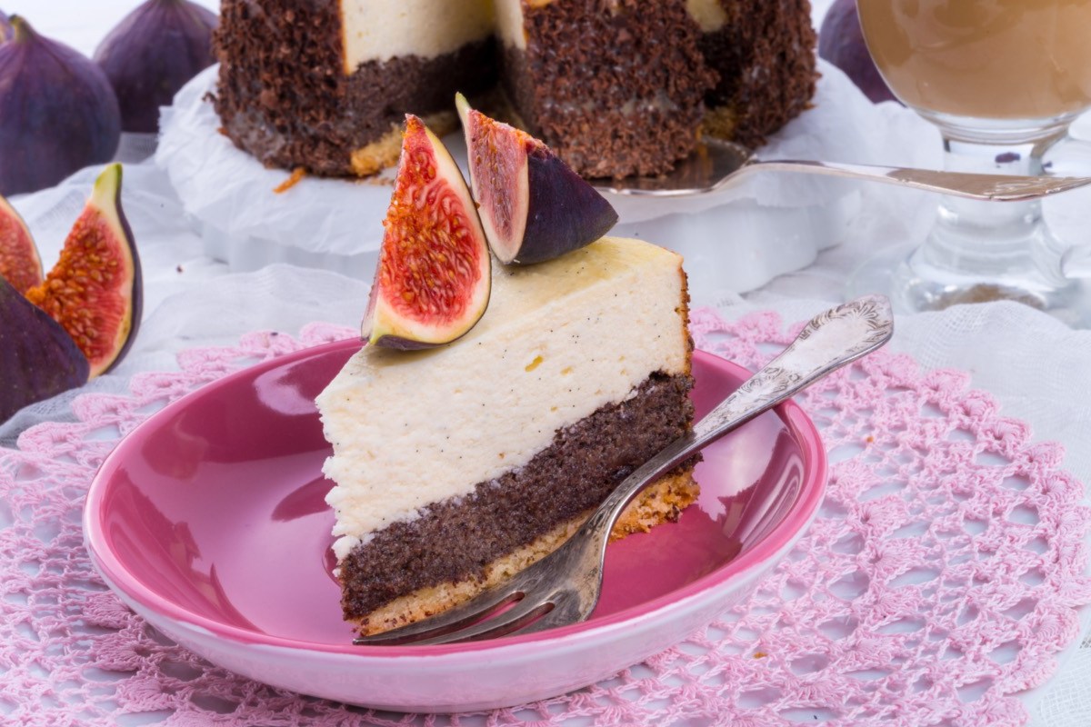 Ein Stück Mohn-Käsekuchen mit Feigen auf einem Teller. Der restliche Kuchen ist im Hintergrund zu sehen.