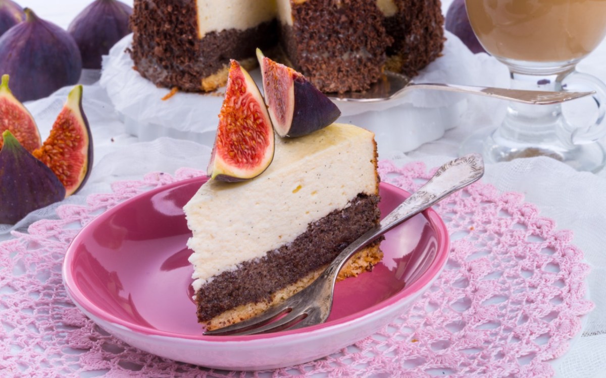 Ein Stück Mohn-Käsekuchen mit Feigen auf einem Teller. Der restliche Kuchen ist im Hintergrund zu sehen.