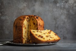 Ein angeschnittener Panettone auf einem Teller vor einem grauen Hintergrund.